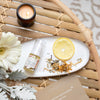 birds eye view of cleansing serum laying flat on a ceramic saucer next to a slice of lemon, some dried tea leaves, a flower and a candle on a flax table