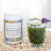 tub of nourish formulated blend on a woven placemat next to a vibrant green glass with a green juice with two sprigs of fresh lavender balancing on the rim