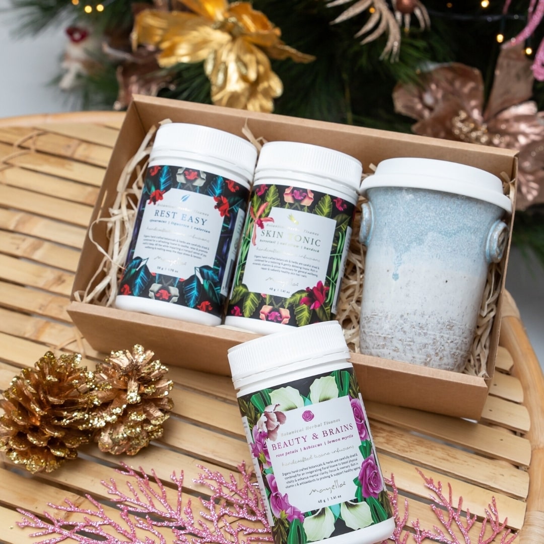 cardboard gift box lined with straw paper with rest easy, skin tonic, beauty and brains and a ceramic travel cup in it