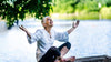 woman sitting by the water happy with her arms up