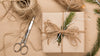 square item wrapped in recycled paper with a twine ribbon and decorated with a sprig of rosemary