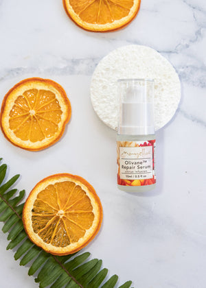 Mayella Olivane Repair Serum - Infusion Citrus 15ml size lying on a grey white marble table with slices of orange, a fern leaf and a white facial sponge