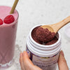 close up of maroon-coloured acai berry beautiful scooped on a wooden spoon next to a pink smoothie in a glass