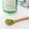 close up of a spoonful of alkalise green and go on a wooden spoon with a tub of alkalise green and go in the background