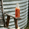 small glass milk jar on a timber outdoor arm chair filled with a reddish coloured iced tea with a bamboo straw inside