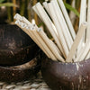 coconut bowl filled with bamboo straws next to a stack of three coconut bowls