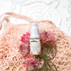 bottle of cleansing lotion laying on pink wild flowers on top of a dusty pink netted shopping bag