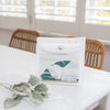 pack of fibre cloths in a mesh bag on a white table with green leaves in front and two chairs and windows behind