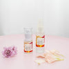 two olivane repair serum citrus infusion bottles side by side in 15ml and 30ml sizes on a light pink table with purple flowers and dusty pink flower petals on either side