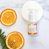 olivane repair serum citrus infusion in the 15ml size laying flat on a marble bench top next to two slices of dehydrated orange and a fern frond