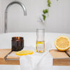 bottle of vitamin c lift serum on a timber bathtub caddy next to half a cut lemon, a lemon slice and a small candle in a brown glass jar