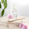 bottle of vitamin A night serum on a pile of four stone tiles with a ceramic spoon in front and surrounded by three lilac flowers