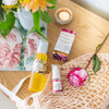 bottle of cleansing serum and olivane repair serum rose infusion on a timber bench top next to a pink rose, a light pink woven shopping tote, a candle and a vase of flowers