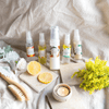 five products in this combination skin set leaning up against a linen-covered cushion surrounded by three stone tiles, two slices of lemon, a dry body brush, two small foliage bunches and a tea candle