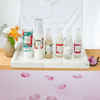 six mayella products in this mature skin set sitting in a marble tray on a timber bath caddy with pink water and rose petals in the bath